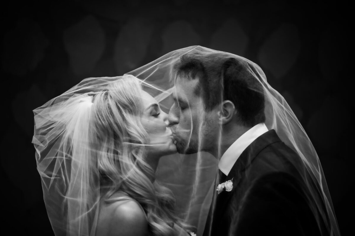 A black and white photo of a bride and a groom kissing under the bride's veil at a Boston Harbor Hotel wedding; photographed by Boston wedding photographers Spagnolo Photography