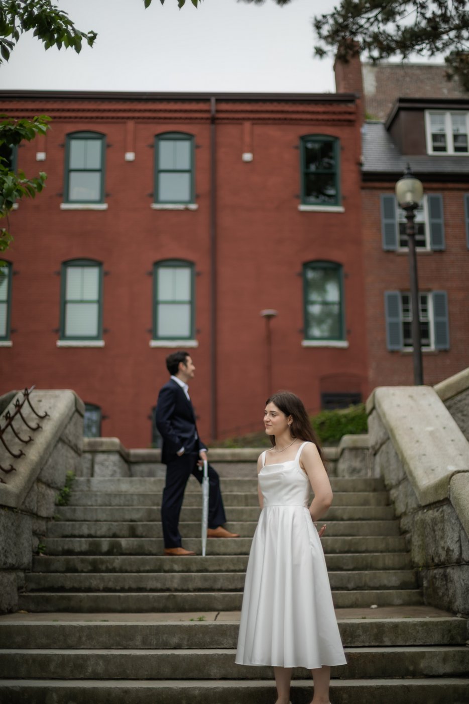 A bride and a groom stand on stone steps in a park, staring off into the distance, photographed during their Boston elopement by Boston wedding Photographers Spagnolo Photography.
