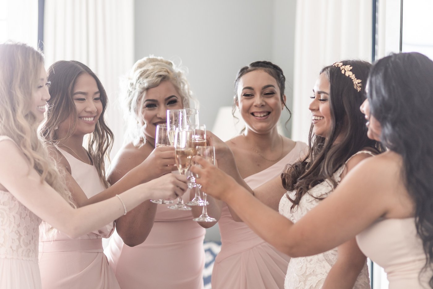 A bride in a white gown and her bridesmaids in pink dresses clink their champagne flutes for a toast before a Cruiseport Gloucester wedding, captured by Boston-based wedding photographers Spagnolo Photography