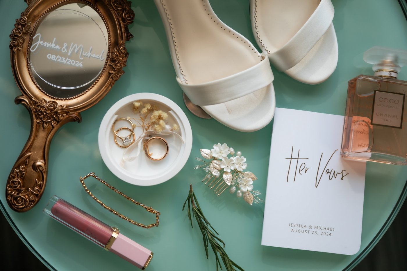 An artistic lay flat of a bride’s wedding day details including shoes, rings, vow book, perfume, and mirror at Oceanview of Nahant.
