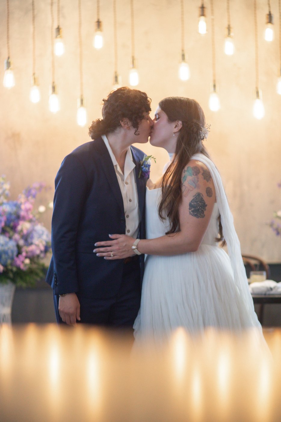 An LGBTQ couple kiss while framed by pale yellow light at their Ledger restaurant wedding in Salem, MA, photographed in a creative, artistic style by inclusive Boston wedding photographers Spagnolo Photography.