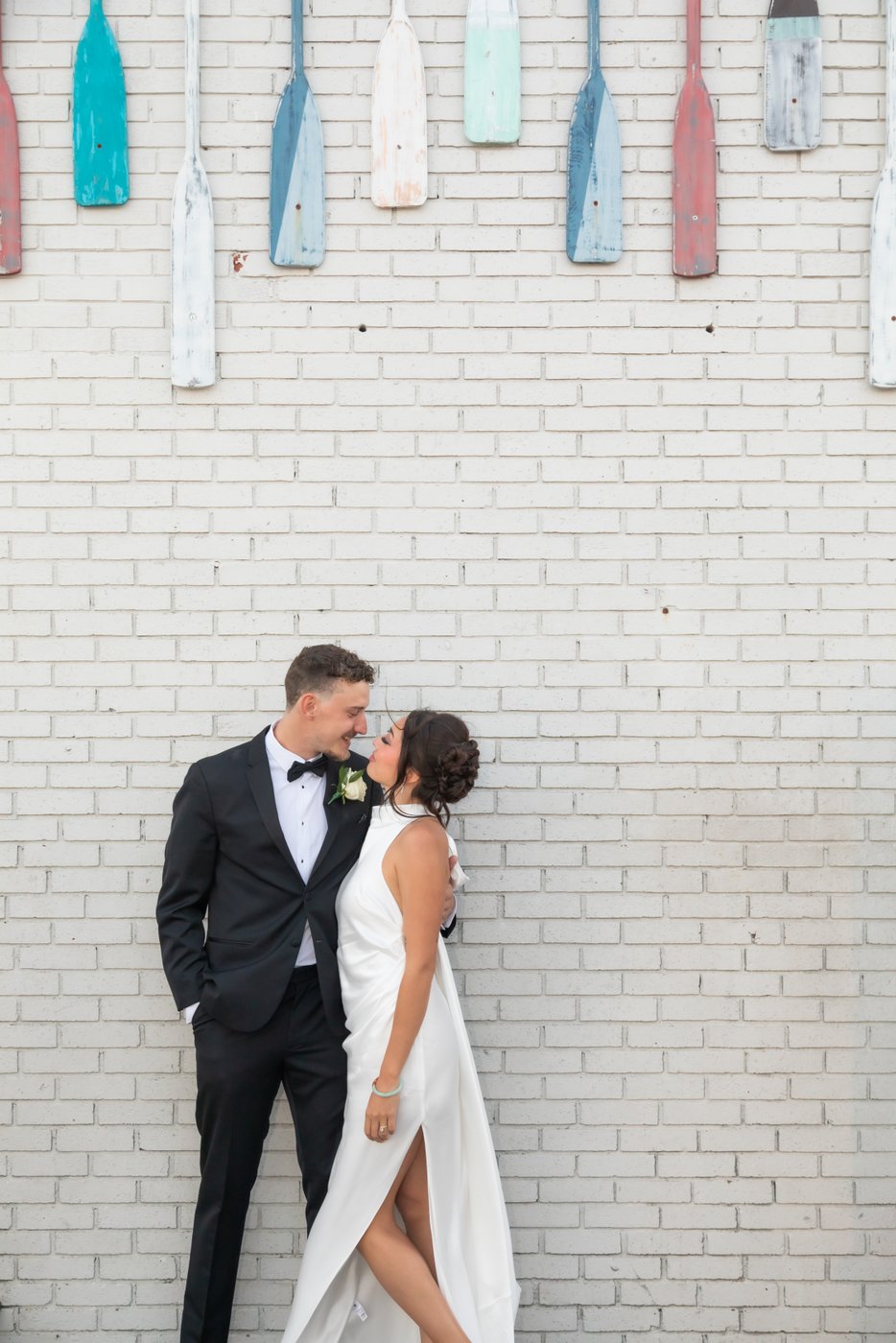 Boston wedding photographers Spagnolo Photography capturing a creative portrait of a bride and a groom standing next to each other and gazing into each other's eyes next to a wall decorated with hanging paddles during their Oceanview of Nahant wedding.