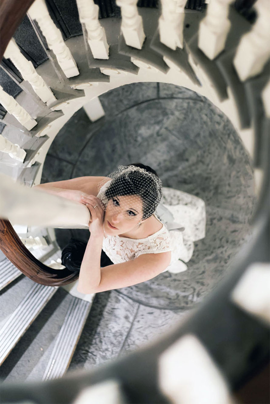 An artistic photograph by Boston wedding photographers Spagnolo Photography of a bride leaning against the ornate stairwell of Boston's historic Old State House and looking up at the camera.