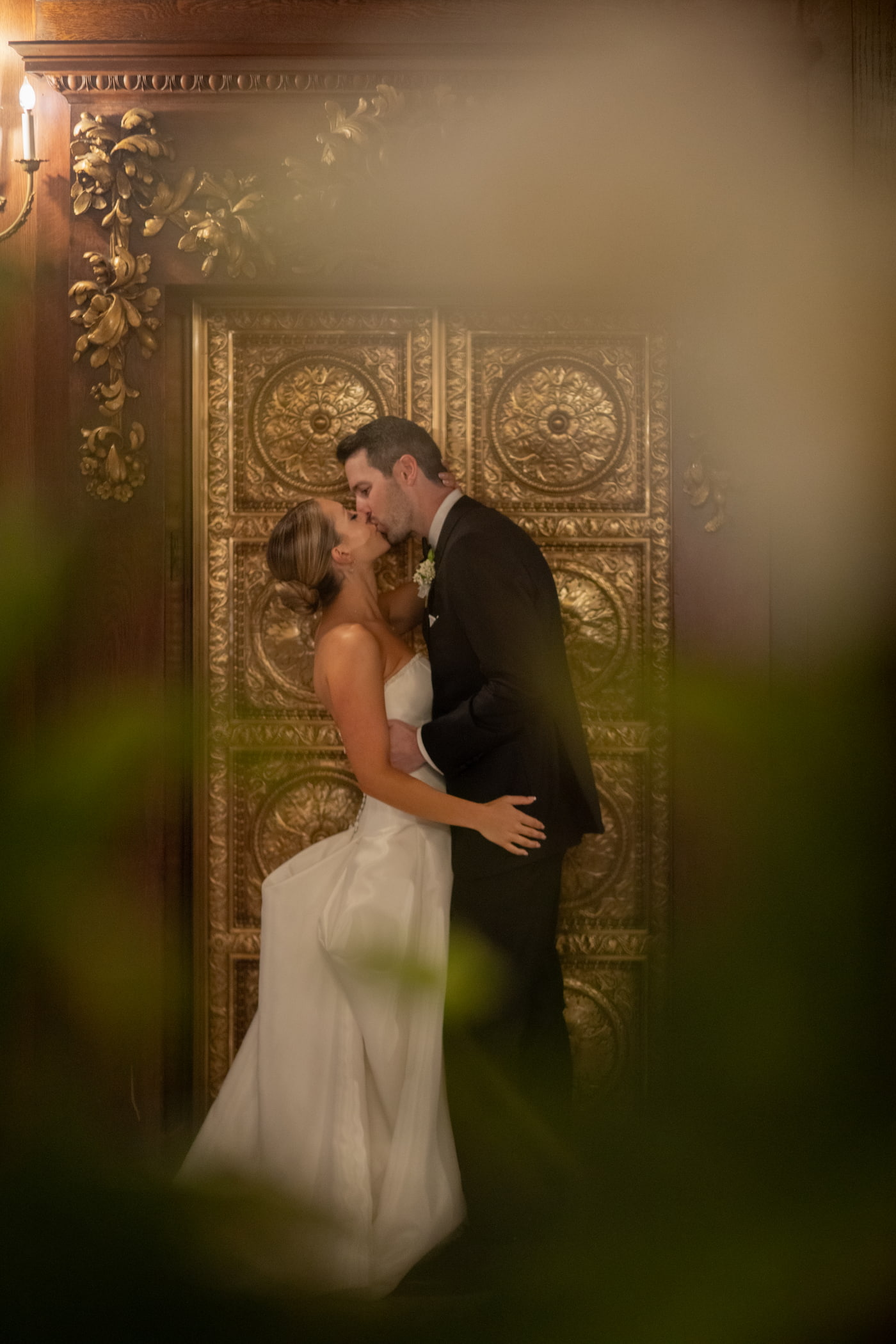 Boston wedding photographers Spagnolo Photography capturing a dramatic and artistic portrait of a bride and a groom kissing in front of the ornate gold elevator of the upscale Omni Parker House hotel in Boston