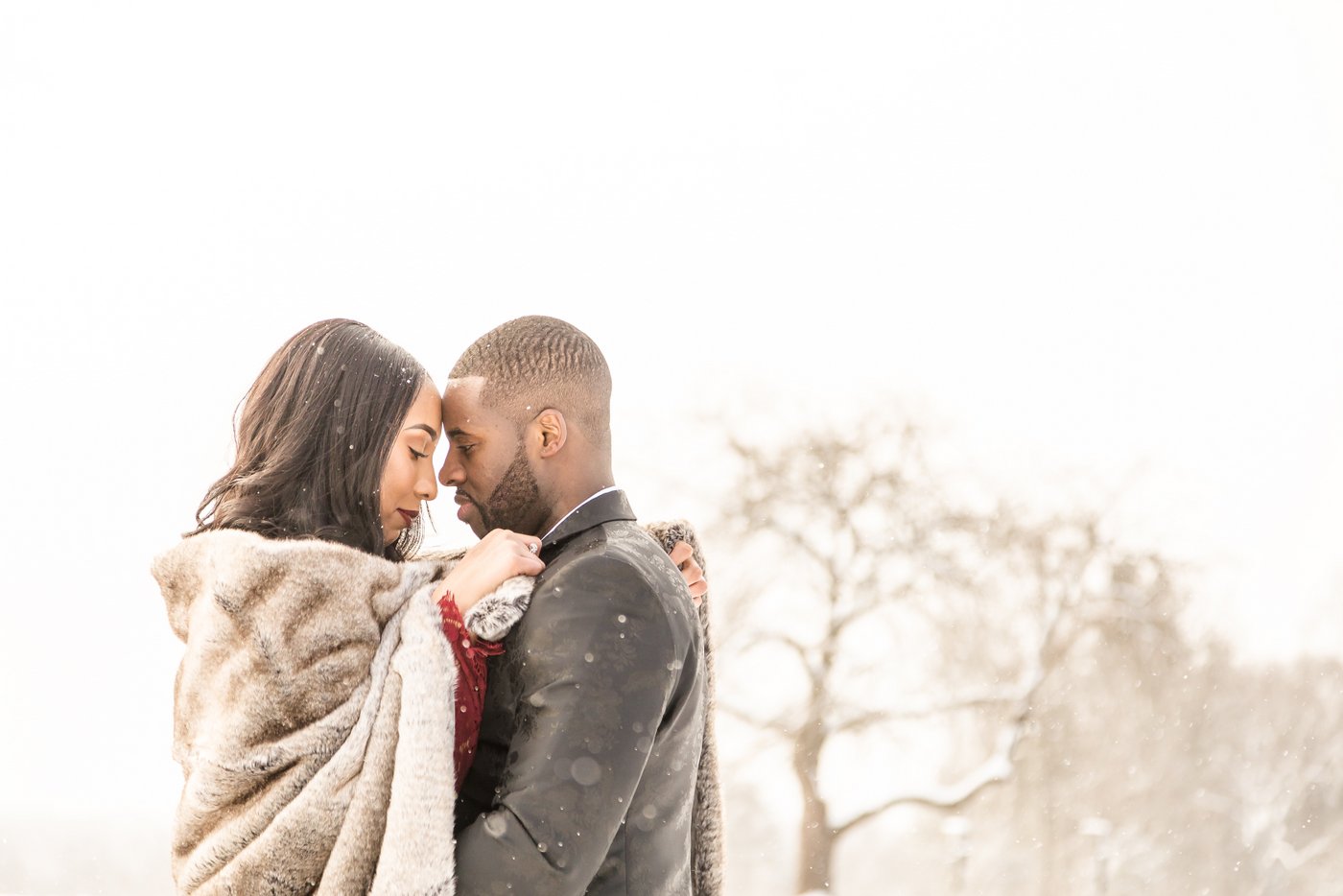 A couple keeping cozy in a blanket during a light snow, photographed on their engagement photography session by Boston wedding and engagement photographers Spagnolo Photography.