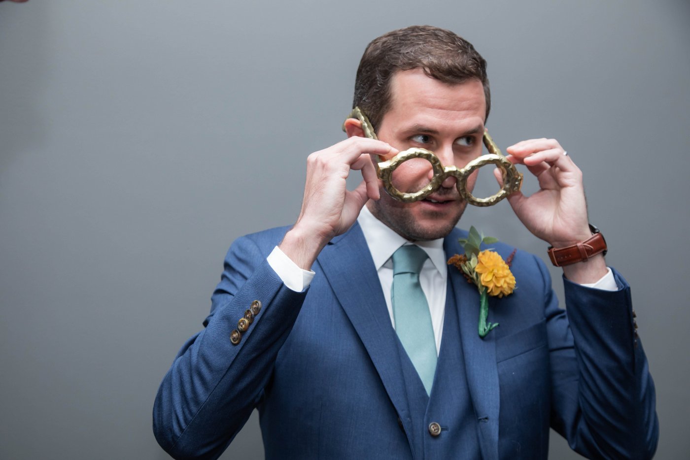 Groom being funny by wearing massive bronze glasses before his fall wedding in Brookline.