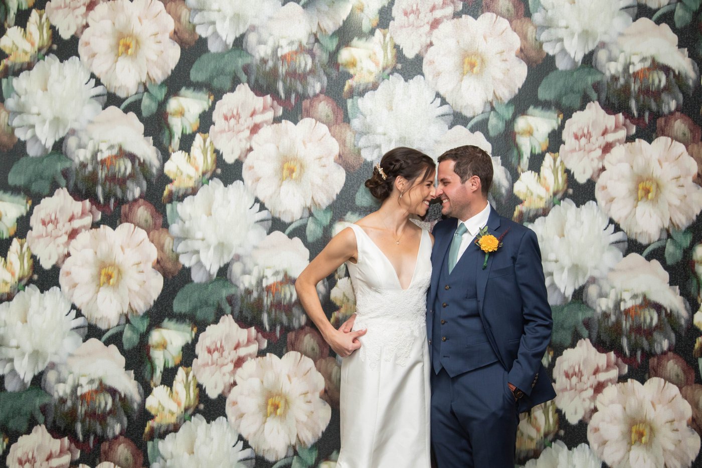 Bride and groom grinning at each other while standing against a floral wallpaper before their fall wedding in Brookline, MA, photographed in a natural candid style by creative Boston wedding photographers Spagnolo Photography