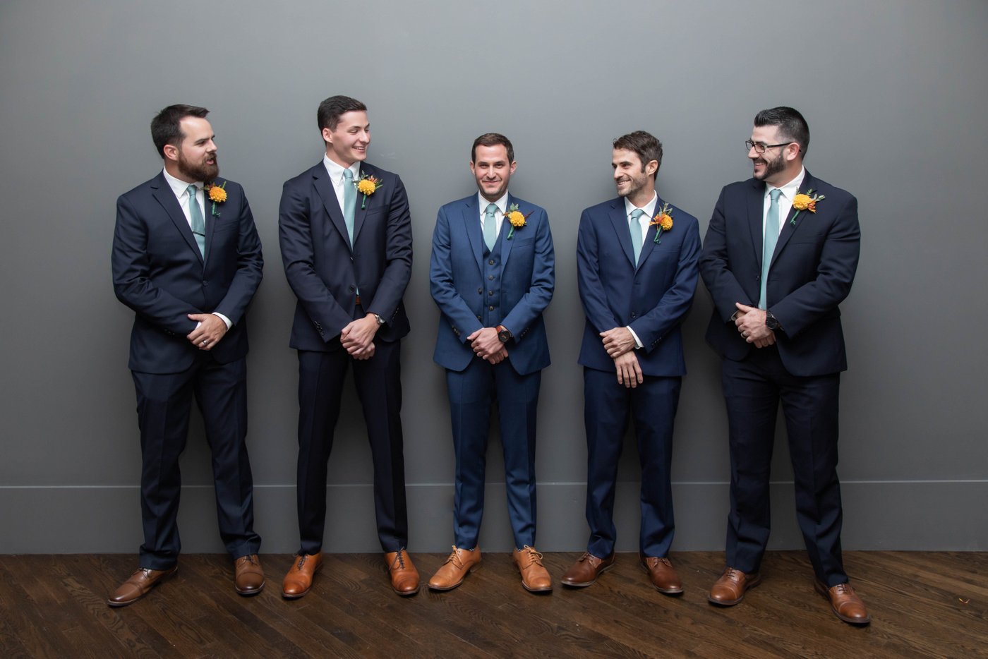 Groom and groomsmen standing against a gray wall at fall wedding in Brookline.