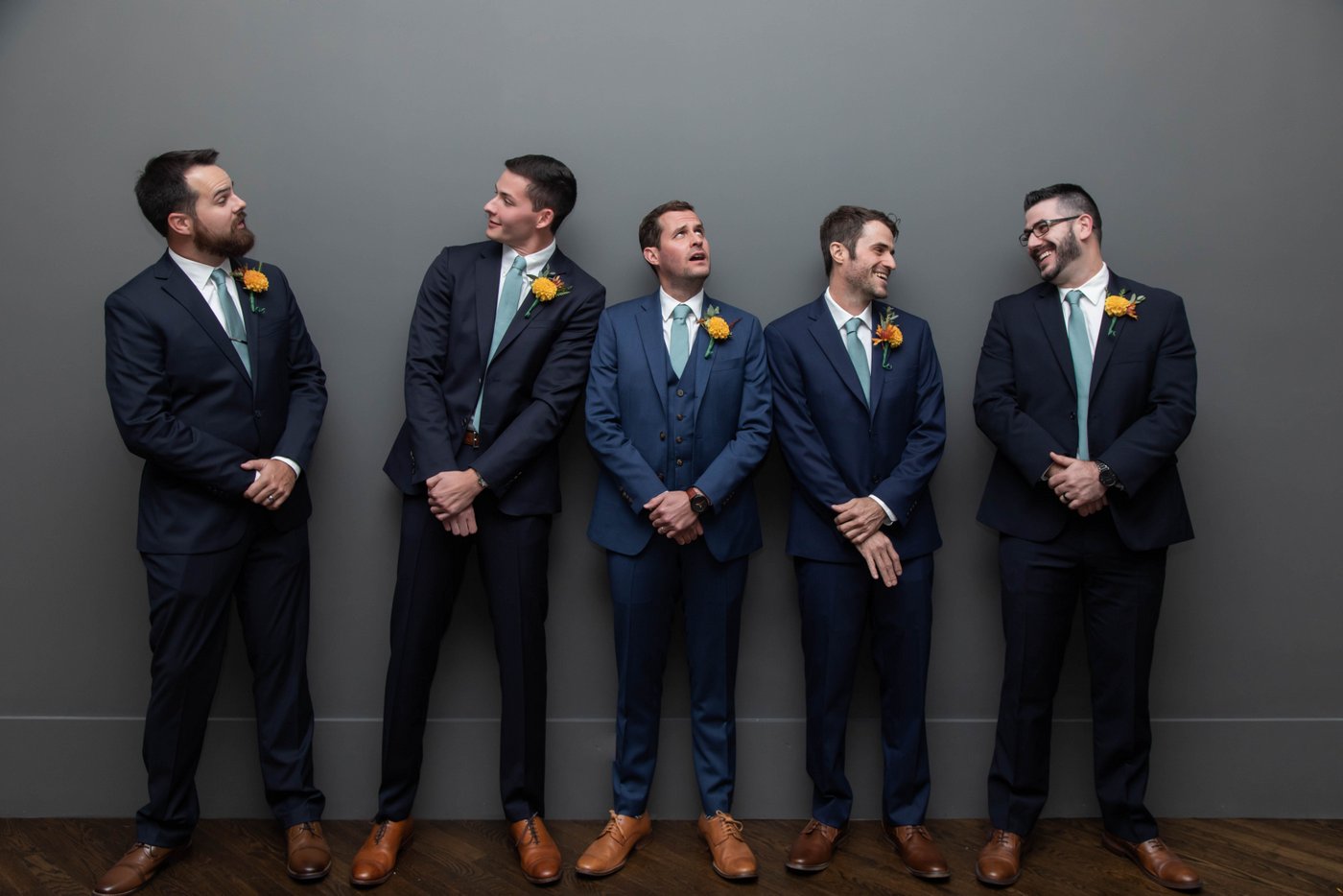 A fun portrait of a groom and his groomsmen standing against a gray wall at fall wedding in Brookline