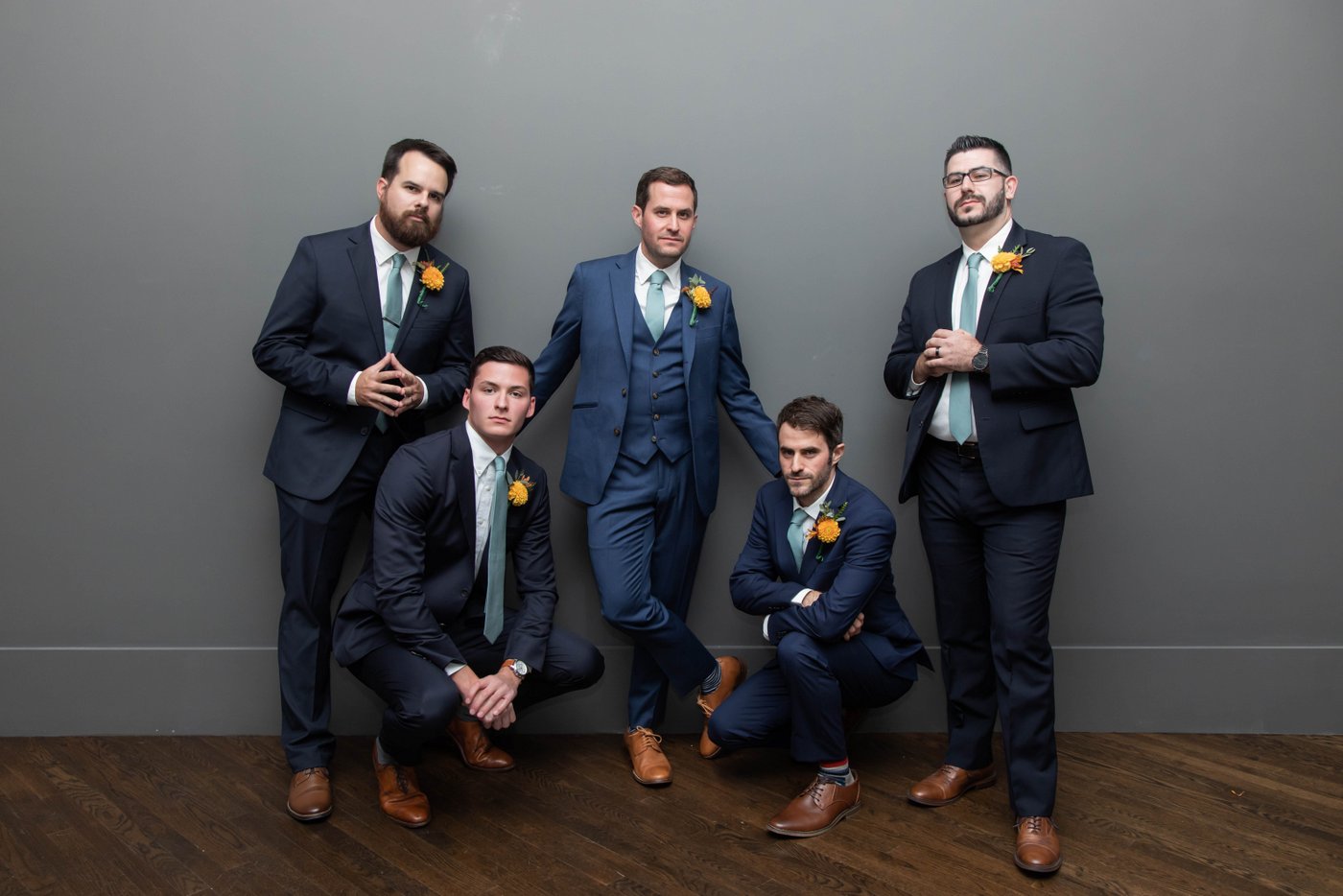 A cool portrait of a groom and his groomsmen striking poses against a gray wall at fall wedding in Brookline, photographed in a cool and edgy style by creative Boston wedding photographers Spagnolo Photography.