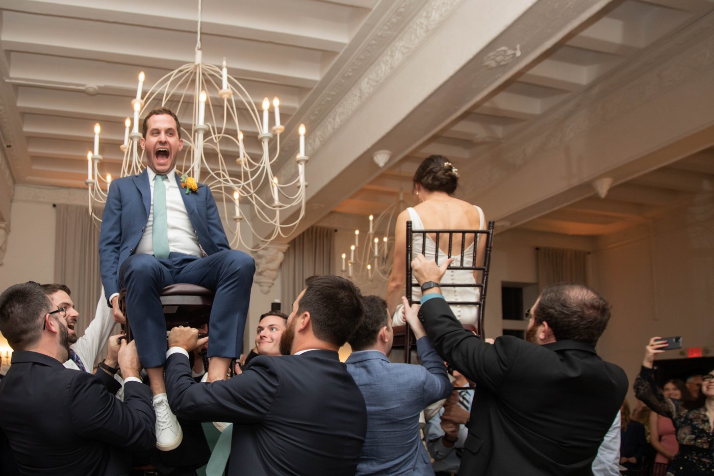 Bride and groom are lifted in their chairs during the Hora dance at an elegant fall Brookline Jewish wedding