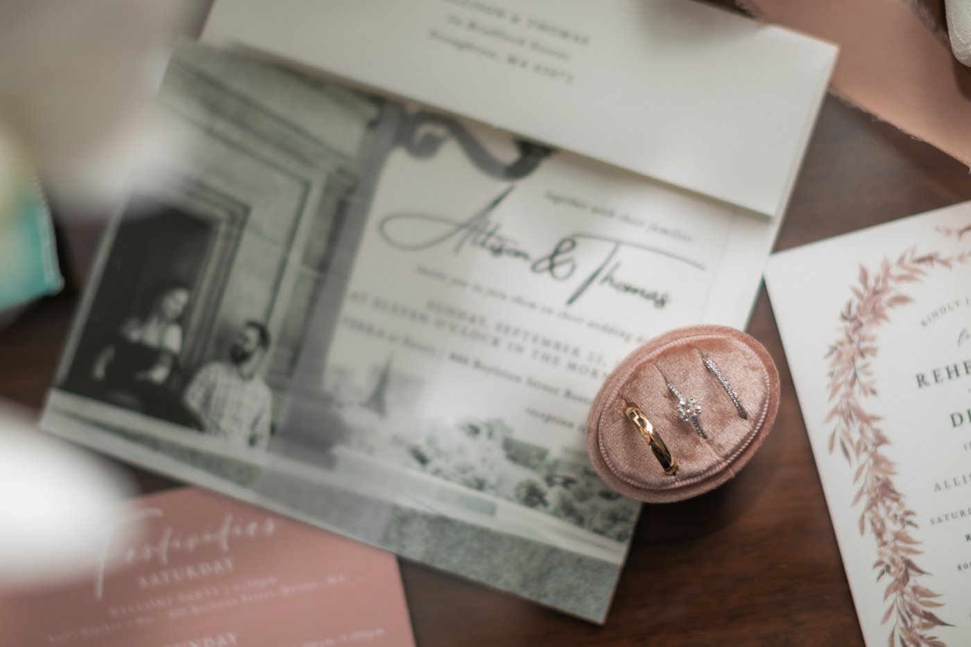 The wedding bands on a pink velvet stand, next to the wedding invitations