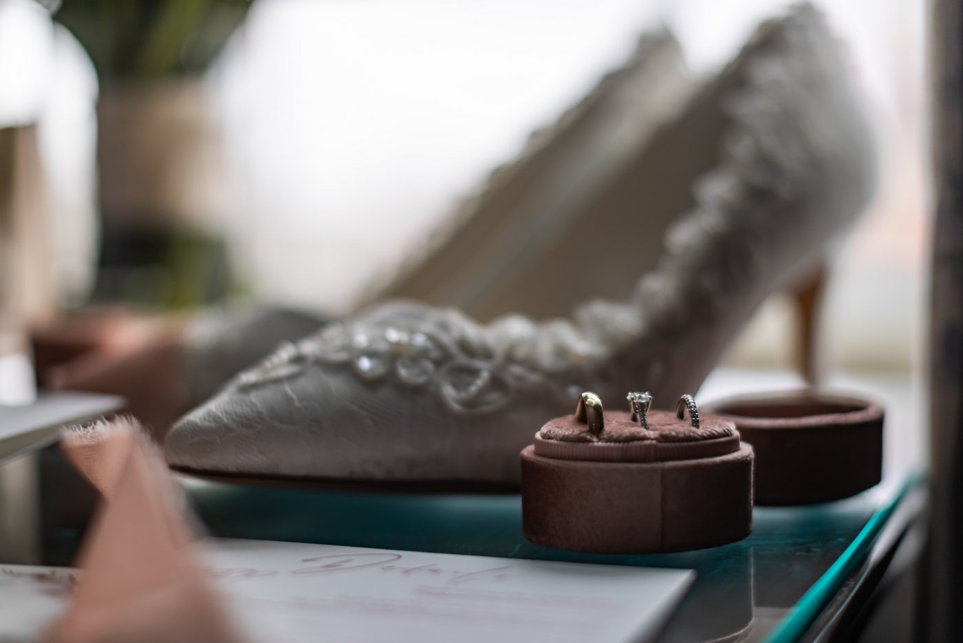 The wedding bands in a pink velvet ring holder, in front of the bride's lacy wedding shoes, photographed at the Eliot Hotel in Boston