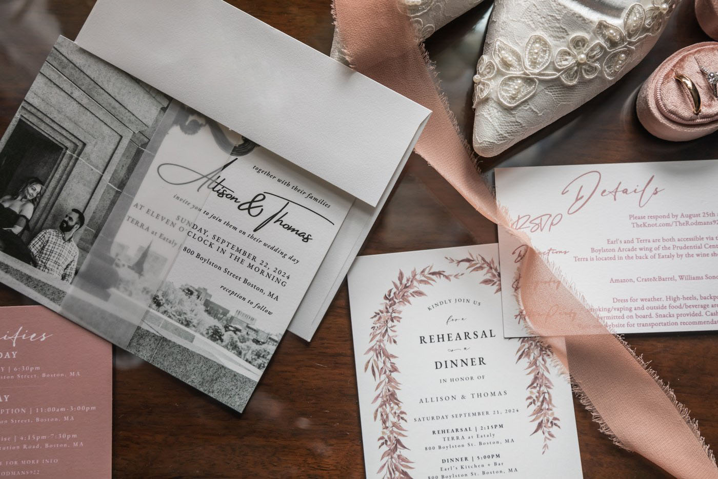 Wedding invitations for a celebration at Terra at Eataly in Boston, a pink ribbon, a white lace wedding shoe, and a pink velvet ring holder with the wedding bands