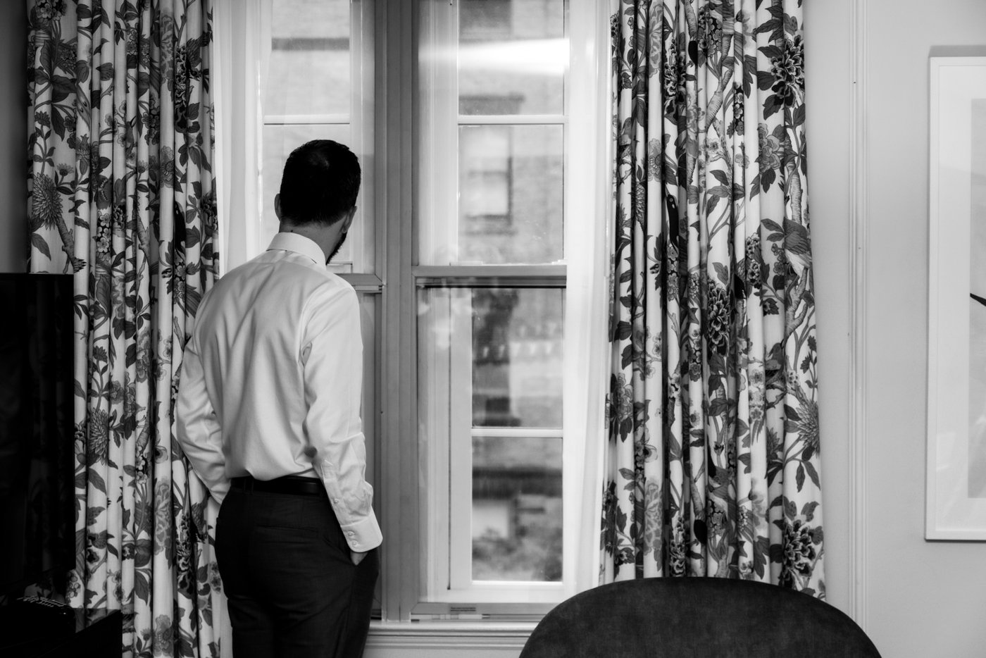 A black and white photo of a groom looking out the window at the Eliot Hotel in Boston, before his Terra Eataly wedding