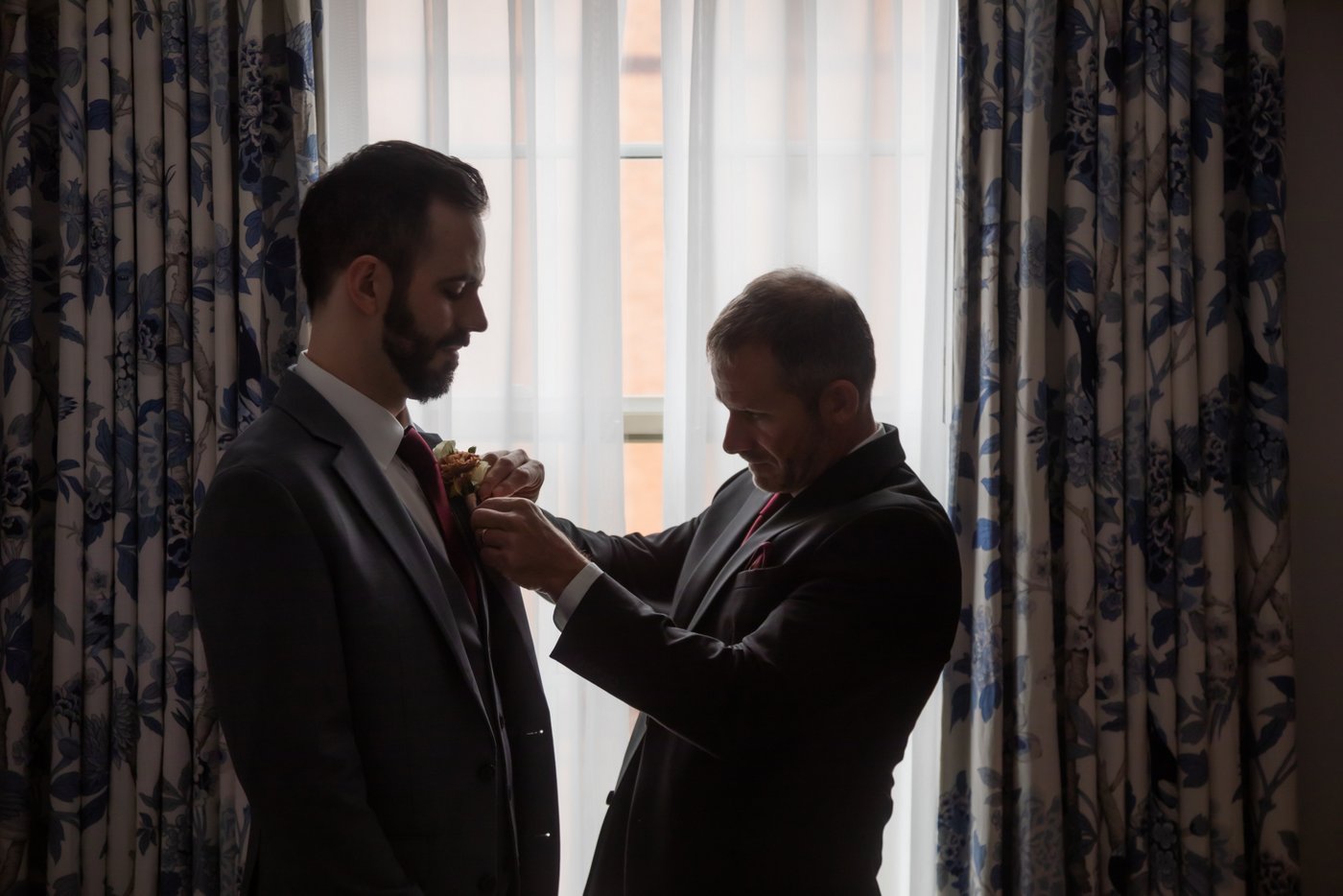 The best man pins the boutonniere to the groom's lapel in the groom's hotel suite at the Eliot Hotel in Boston