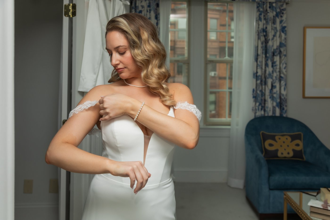 The bride adjusts the strap of her wedding dress in her bridal suite at the Eliot Hotel in Boston