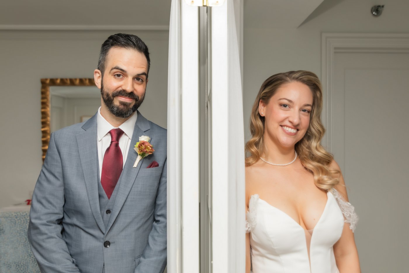 A bride and a groom smile at the camera while separated by a wall, before their Boston wedding