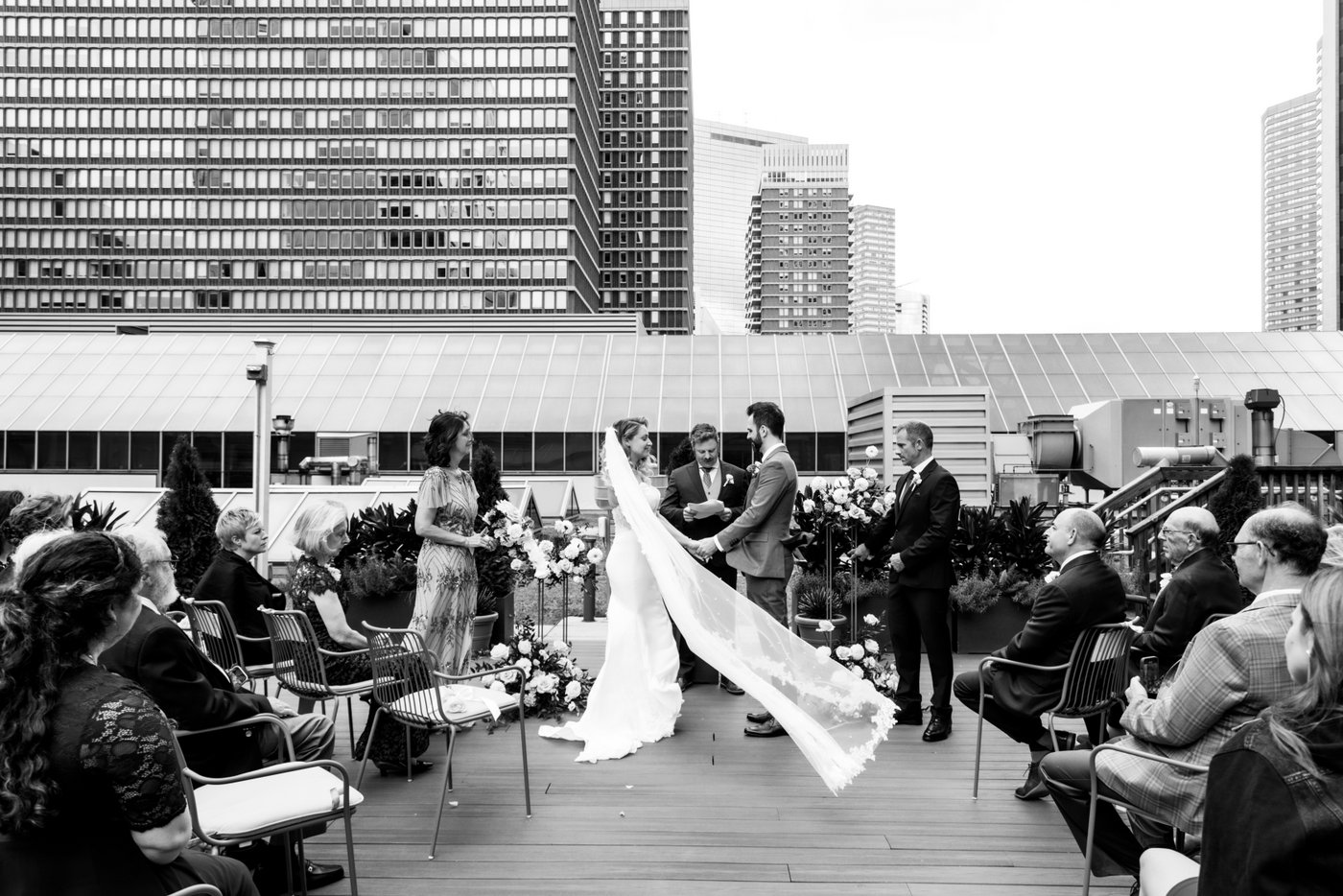 A black and white photo of the bride and groom holding hands as the bride's veil blows in the wind during their rooftop micro wedding ceremony at Terra at Eataly in Boston