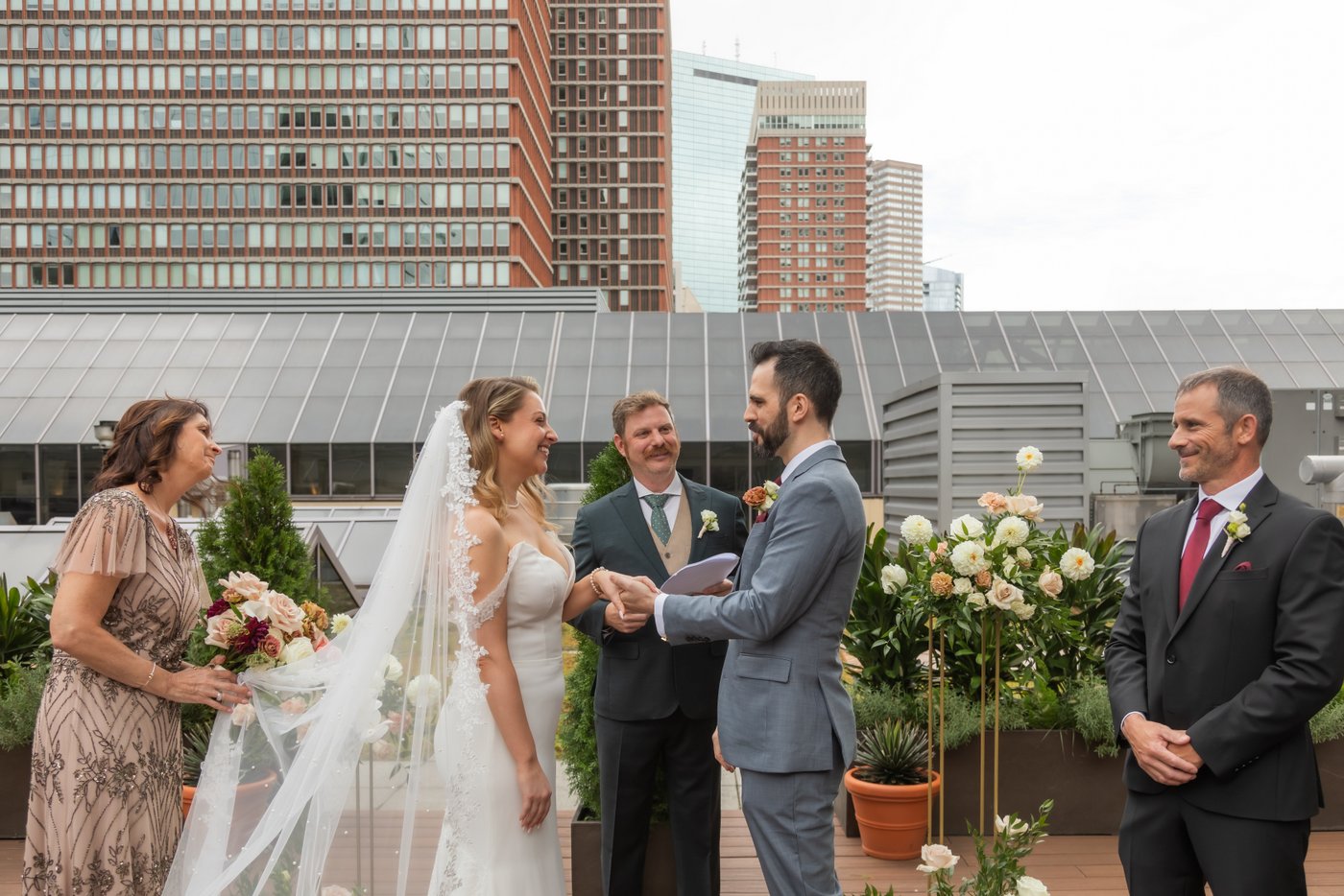 The bride and groom smile at each other as they exchange rings during their rooftop wedding ceremony at Terra at Eataly in Boston