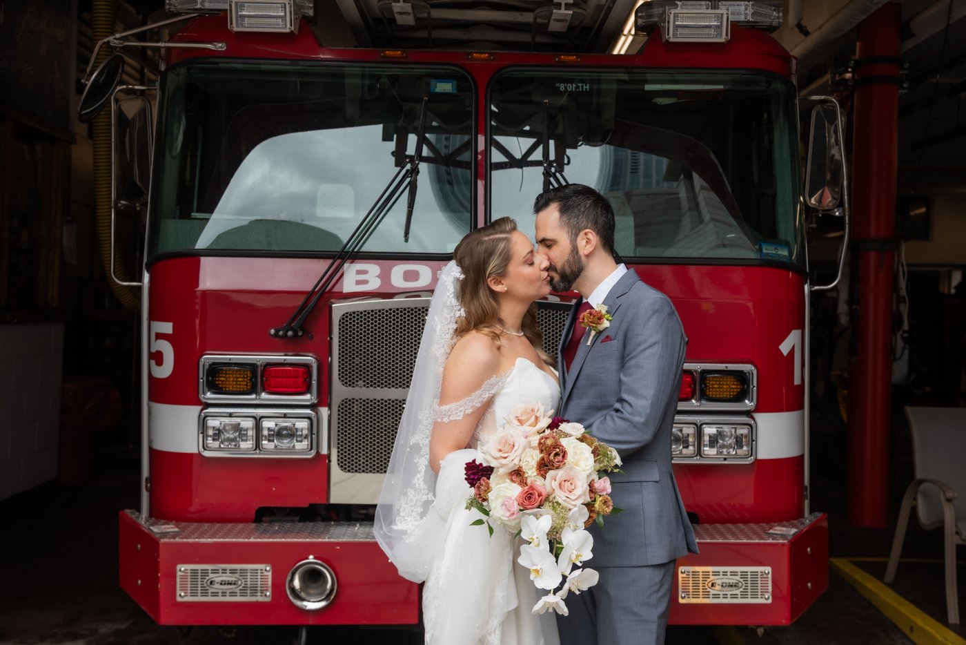 A bride and a groom kiss in front of a fire truck parked in the fire house in Boston's Back Bay during their Terra Boston wedding at Eataly, photographed by Boston micro wedding photographers Spagnolo Photography in a natural, candid style.