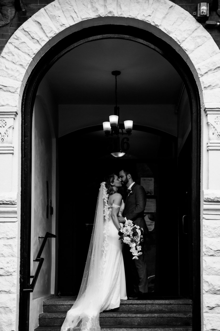 A black and white photo of a bride and a groom kissing in the entryway of a building in Boston's Back Bay neighborhood
