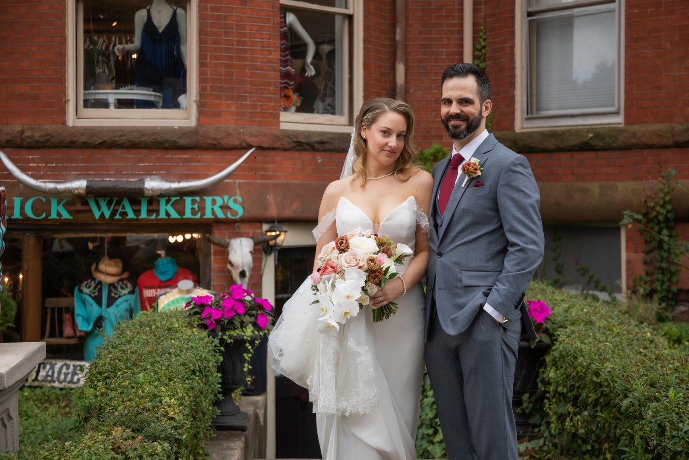 A bride and a groom pose in front of Rick Walker's shop on Newbury Street in Boston's Back Bay, during their wedding portraits along Boston Streets, following their Terra at Eataly wedding ceremony