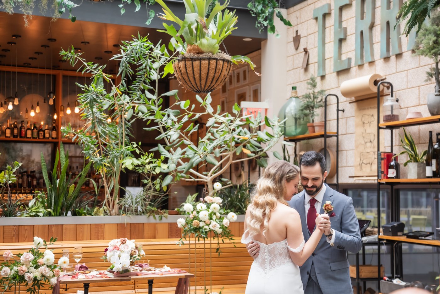 The bride and groom during their first dance surrounded by lush green plants under the "Terra" sign at their Terra at Eataly wedding in Boston