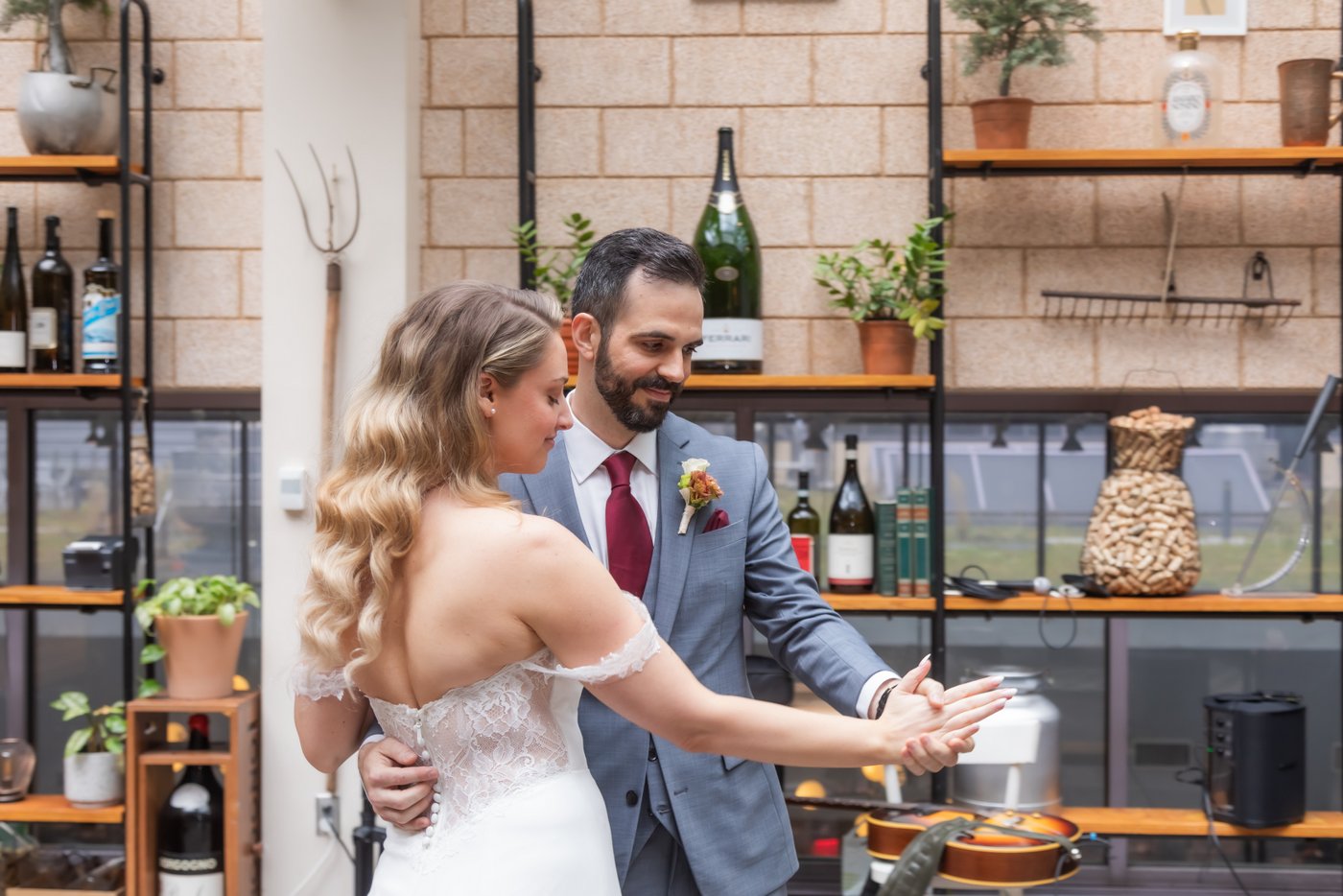 The bride and groom dance near a wall decorated with wine bottles, plants, and gardening tools at their Terra at Eataly wedding in Boston