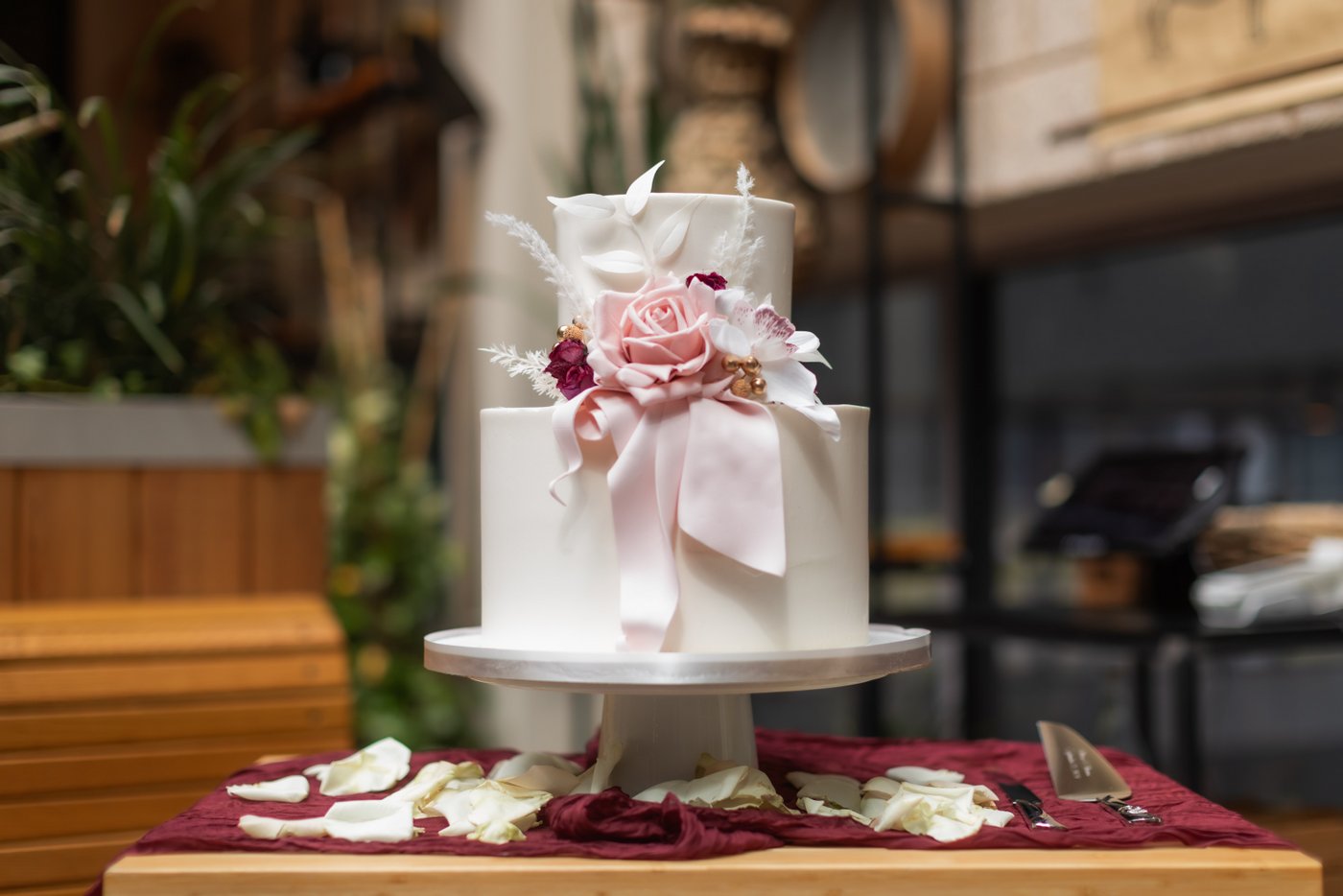 A beautiful white two-tiered wedding cake with a rose and ribbons made of pink fondant at a micro wedding at Terra at Eataly.