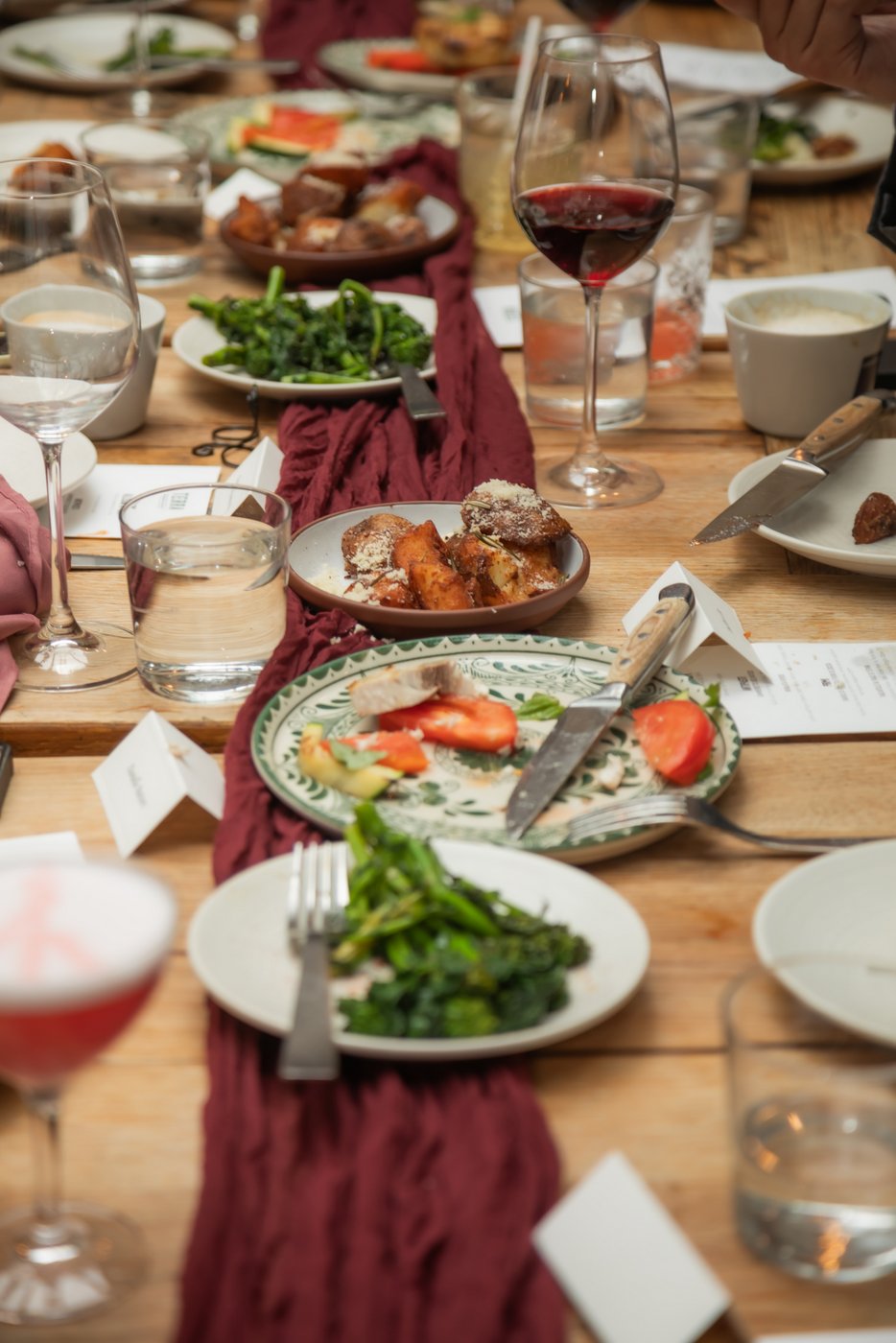 A table with a burgundy linen table runner and plates of food and wine glasses at a Terra Boston wedding