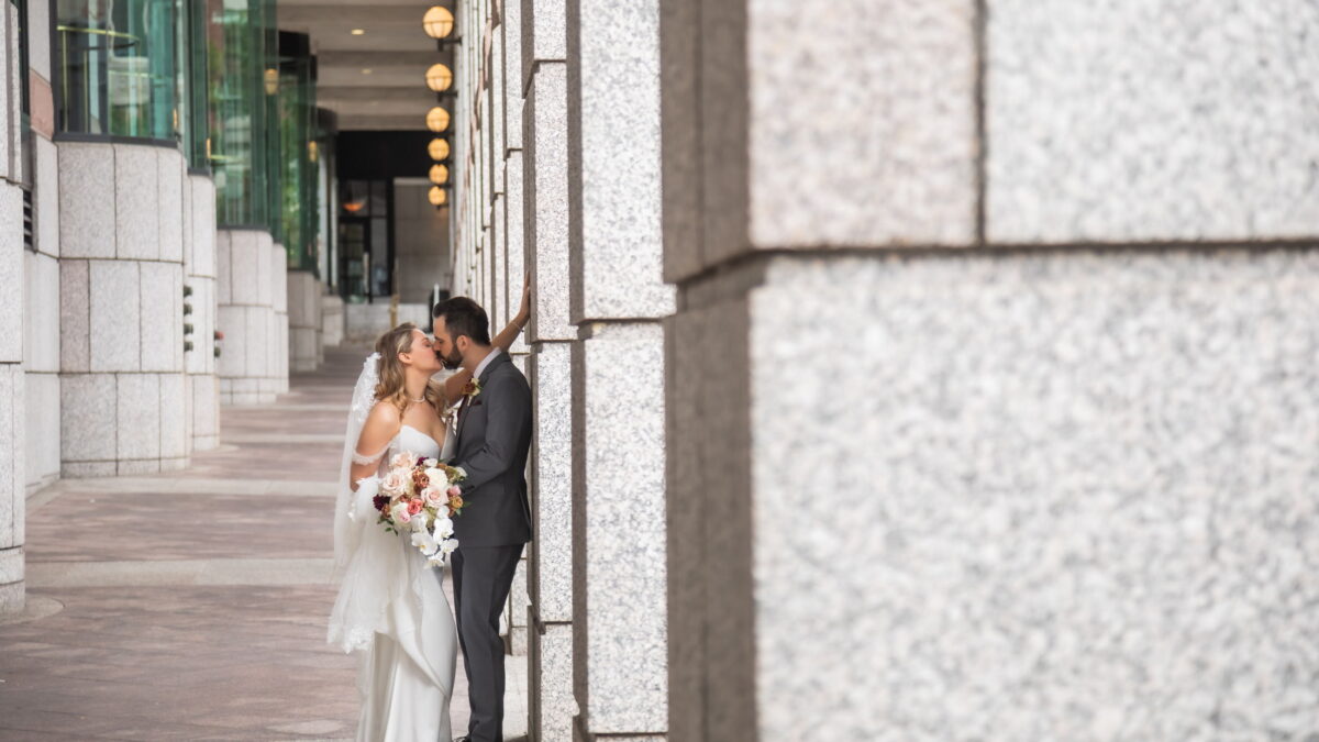 A bride and a groom kiss by stone columns in Boston's Back Bay during their Terra Boston wedding at Eataly, photographed by Boston micro wedding photographers Spagnolo Photography in a natural, candid style.