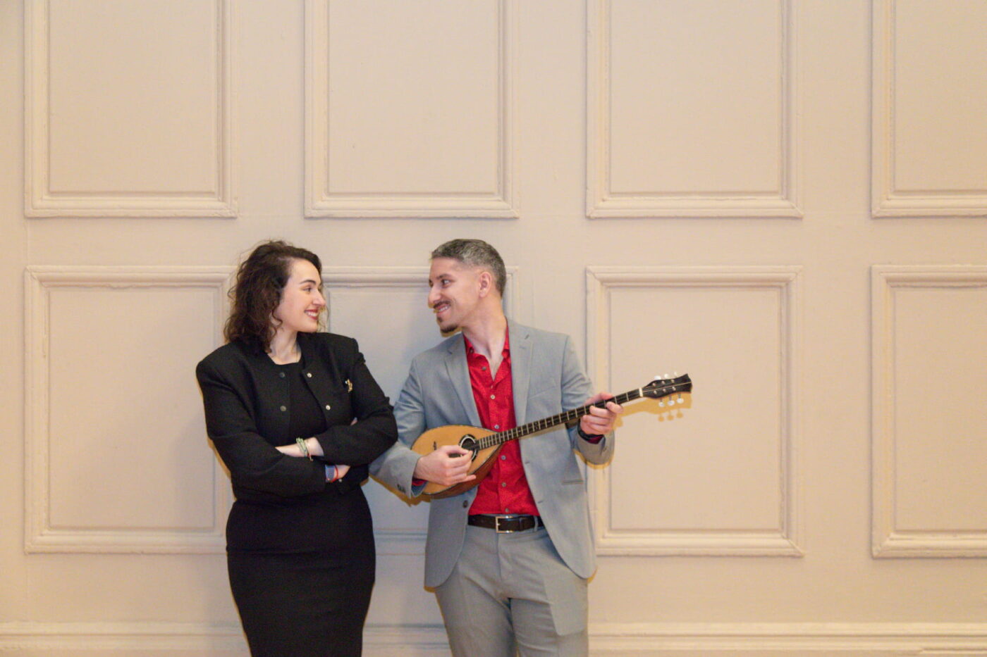 A Boston Symphony Hall engagement photo of a man playing the Greek Tzouras as a woman in a black dress looks at him lovingly, photographed by Boston engagement photographers Spagnolo Photography in 2025, and featured on their blog.