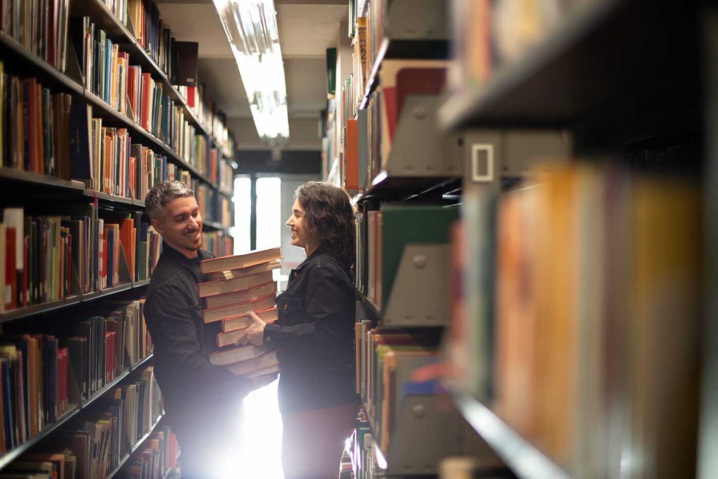 A Boston engagement photo of a woman and a man holding a large stack of books at Boston University's Library during their 2025 engagement photoshoot by Spagnolo Photography