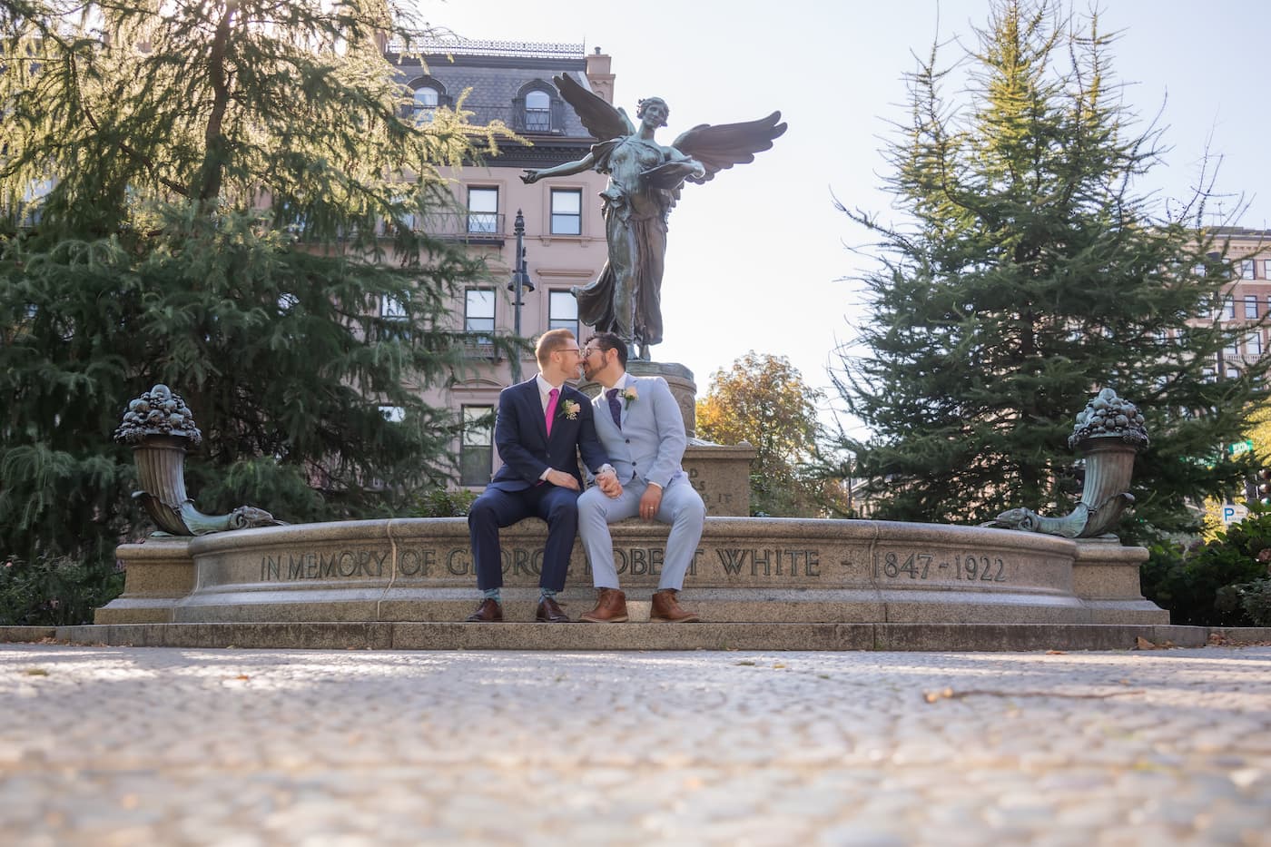 Two grooms sit at the edge of a fountain and kiss during their wedding elopement at the Boston Public Garden, photographed by LGBTW friendly Boston elopement photographers Spagnolo Photography