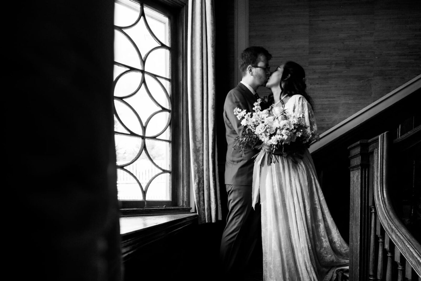A black and white photo of a bride and a groom kissing on the stairs of the Endicott Estate in Dedham, MA
