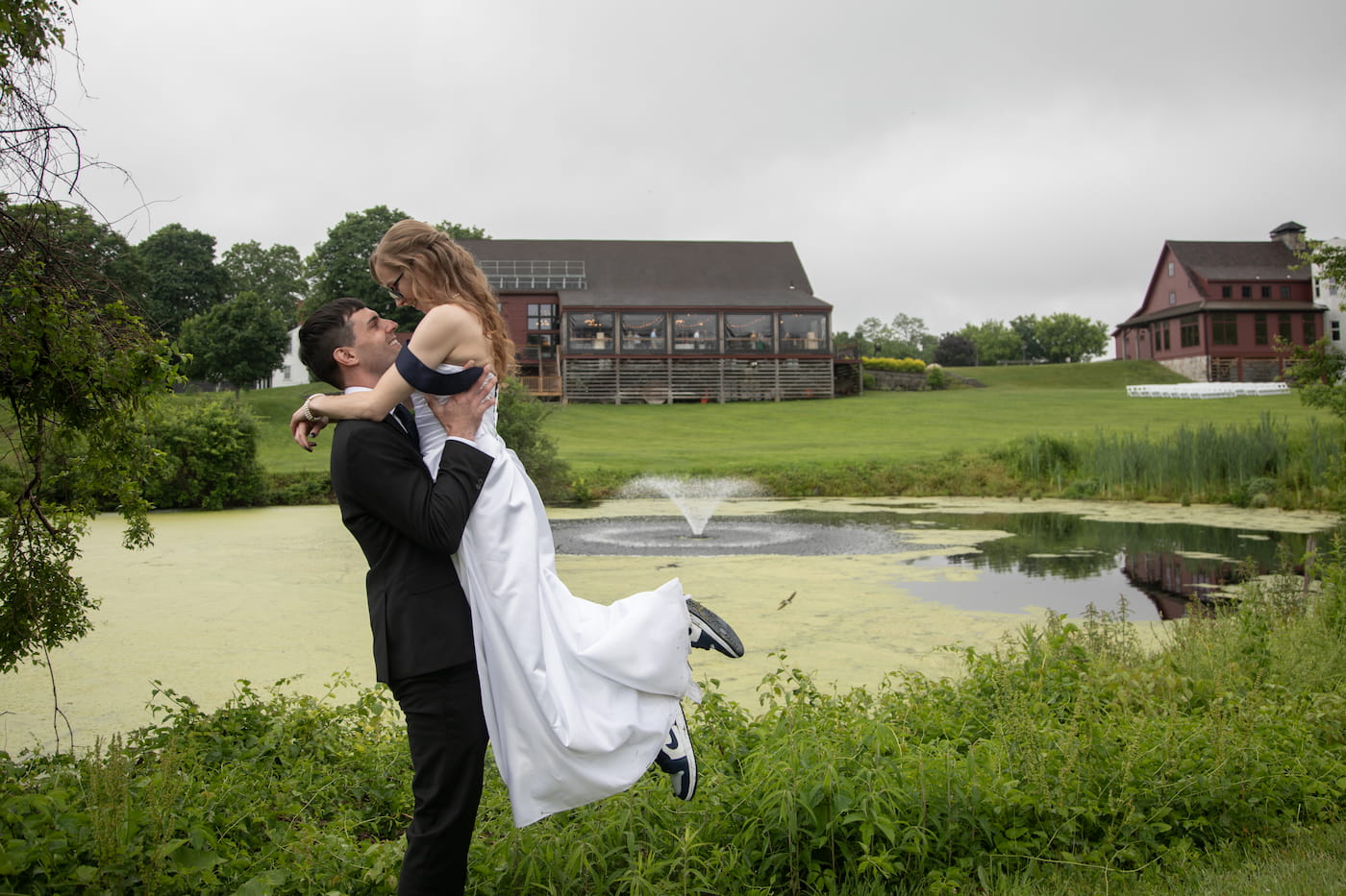 A groom picks up a bride as they kiss by the pond at the Barn at Gibbet Hill during their wedding