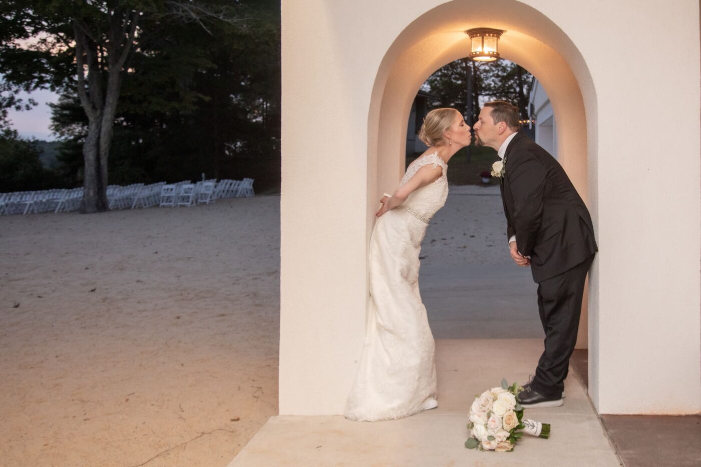 A bride and a groom kiss  at the boathouse of Lake Pearl Wrentham on their wedding day at sunset.