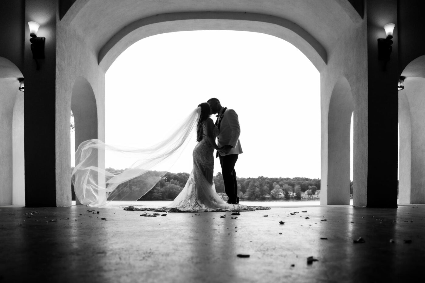 A black and white photo of a bride and a groom kissing while the bride's veil floats behind her in the boathouse of Lake Pearl Wrentham on their wedding day