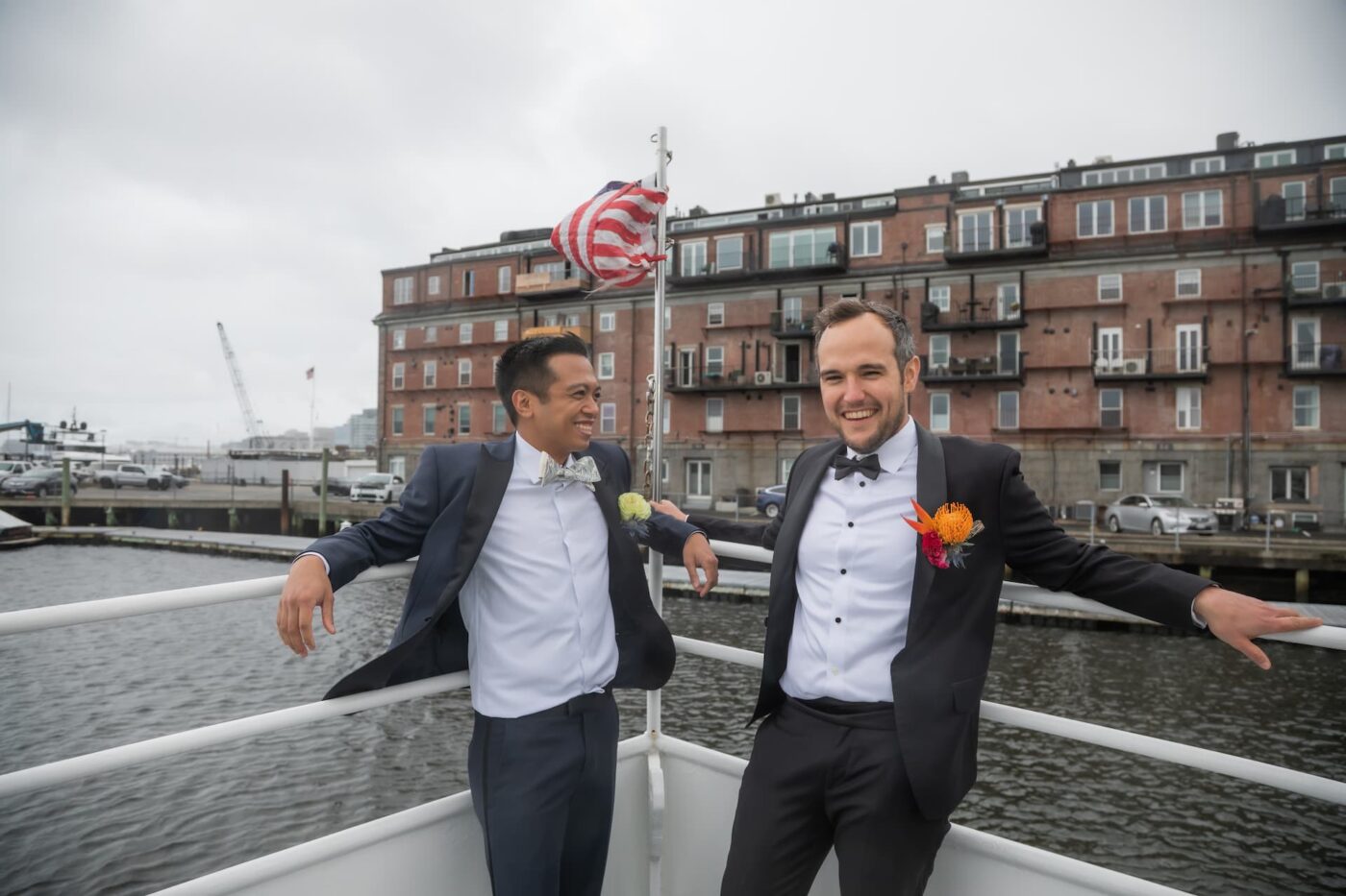 Two grooms on the deck of a boat in the Boston Harbor on their wedding day, which was later held at the New England Aquarium