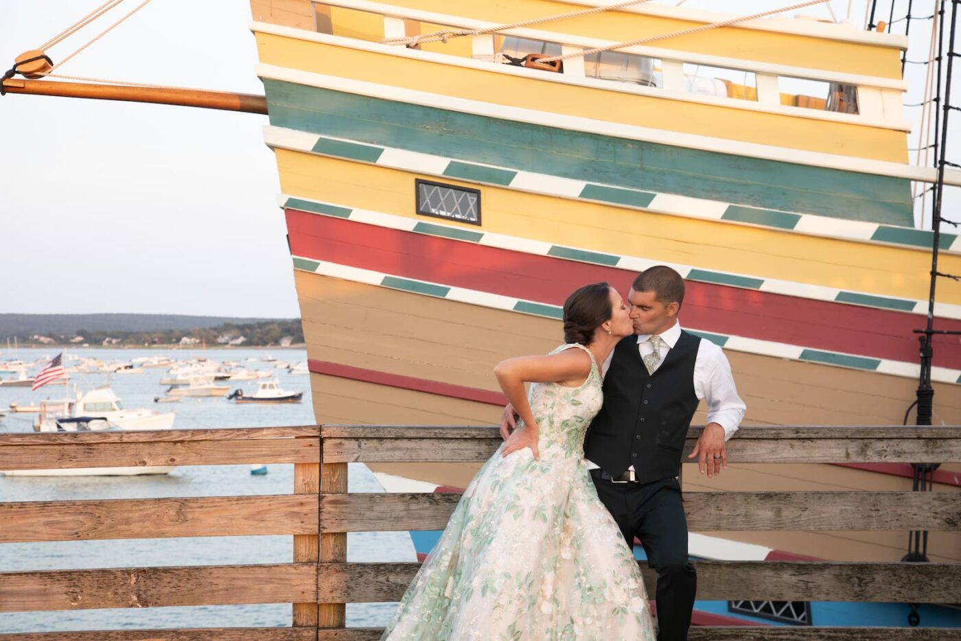 A bride and a groom kiss next to a colorful ship during their wedding at 71 West Atlantic Steakhouse in Plymouth, MA