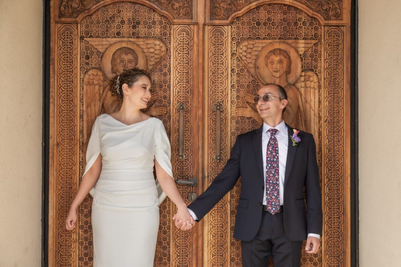 A couple stands in front of the ornate wooden doors of an Armenian Orthodox Church in Washington DC on their wedding day.