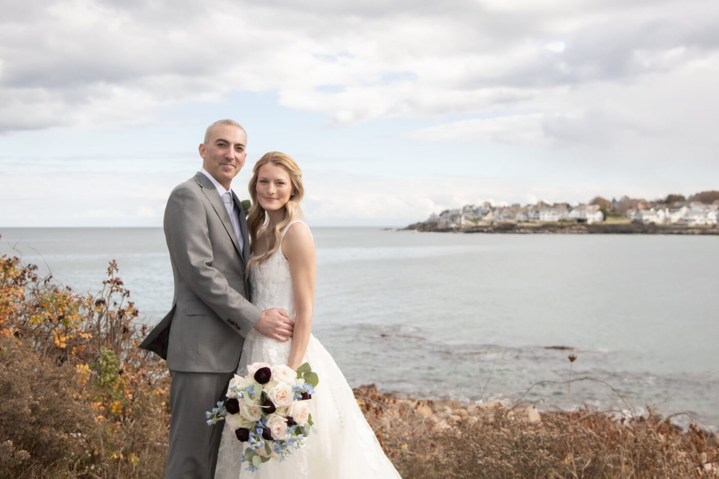 A bride and a groom pose for the camera in front of the ocean during their Union Bluff Hotel & Meeting House wedding in York, Maine