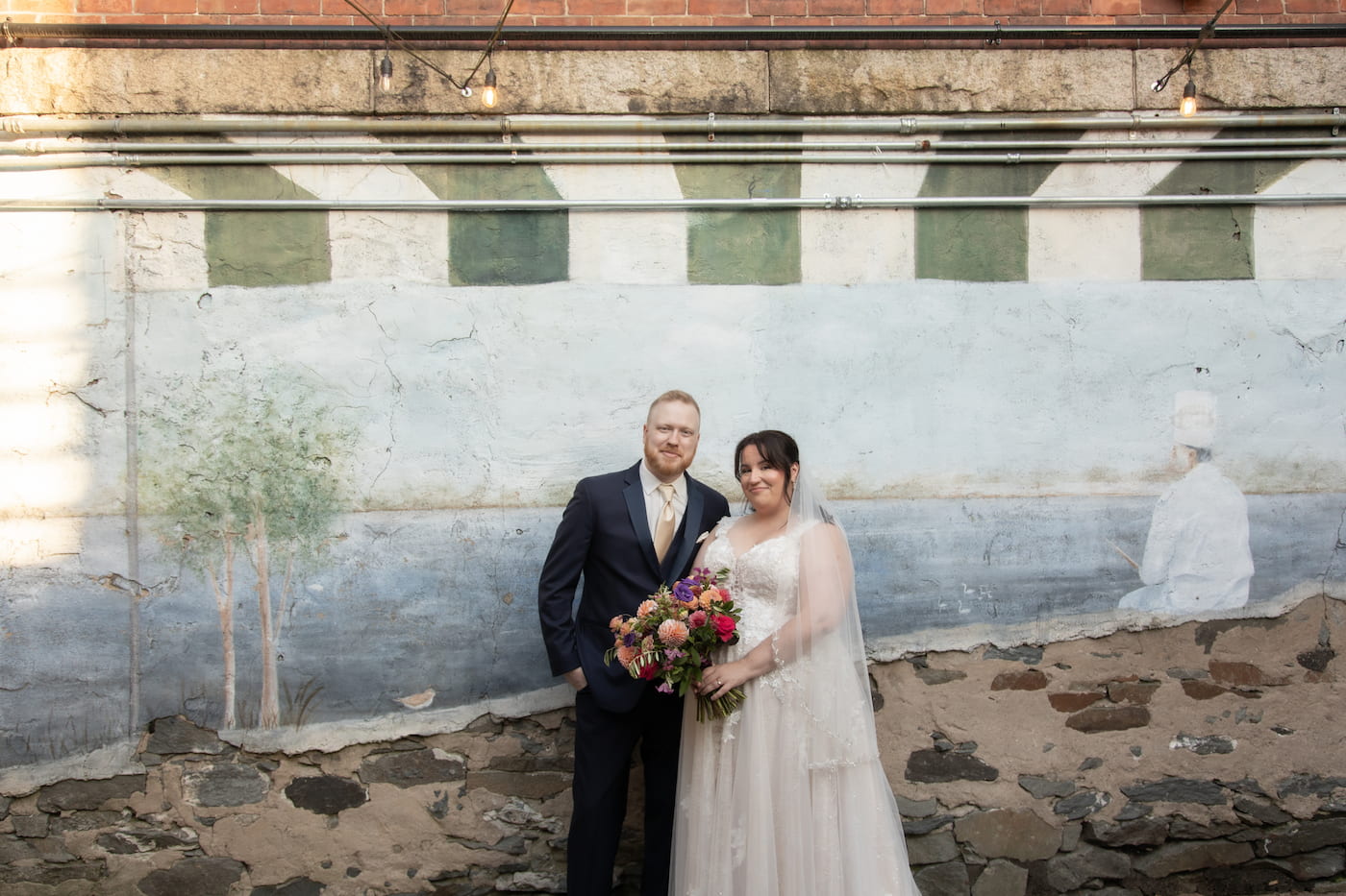 A bride and a groom pose in front of a beautiful chipped mural outside the Waterman Grille in Providence, Rhode Island, on their wedding day