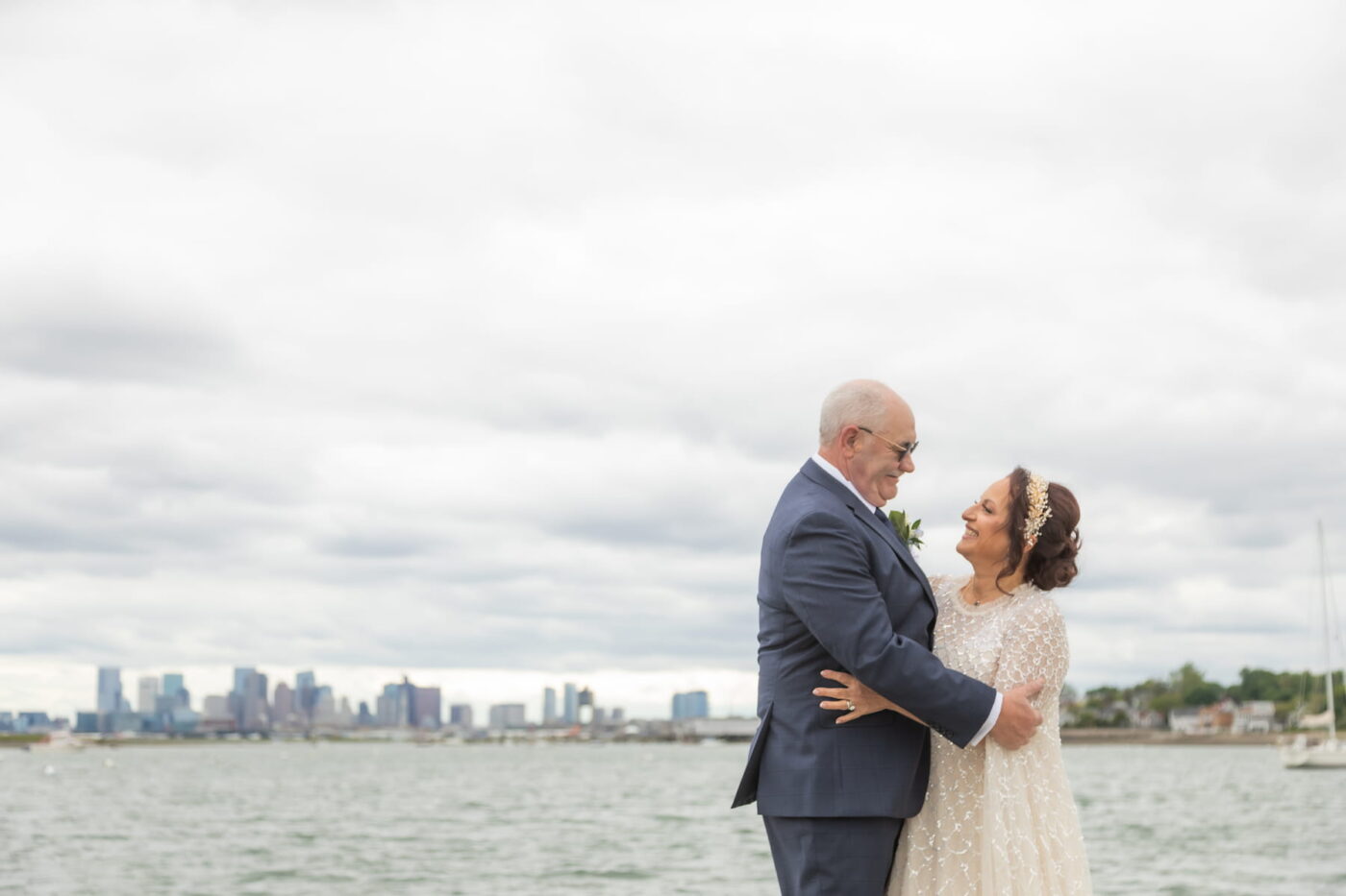 A bride and a groom smile at each other as they stand by the ocean during their Winthrop Yacht Club wedding