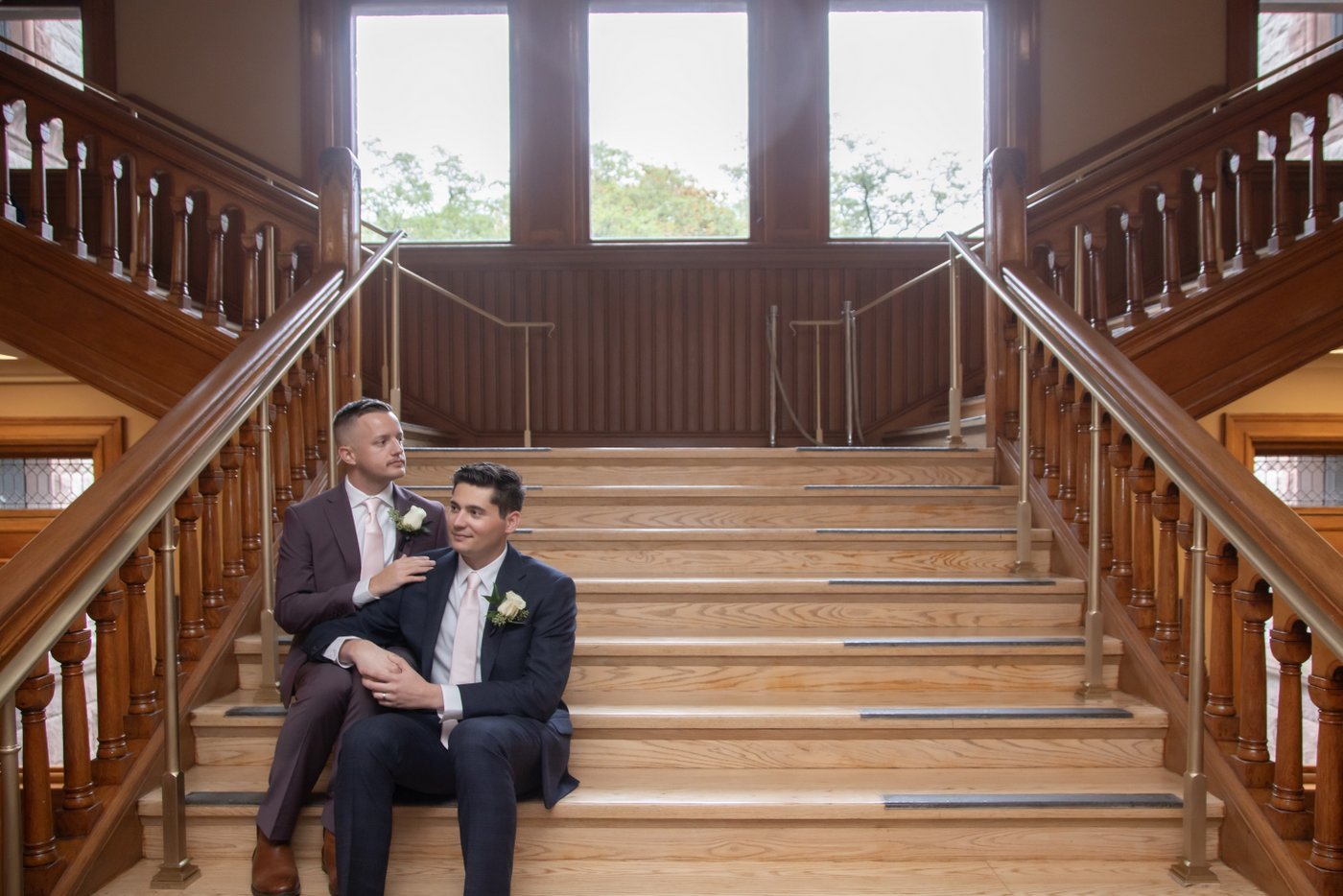 Two grooms sitting on the stairs of Cambridge City Hall, waiting to get married