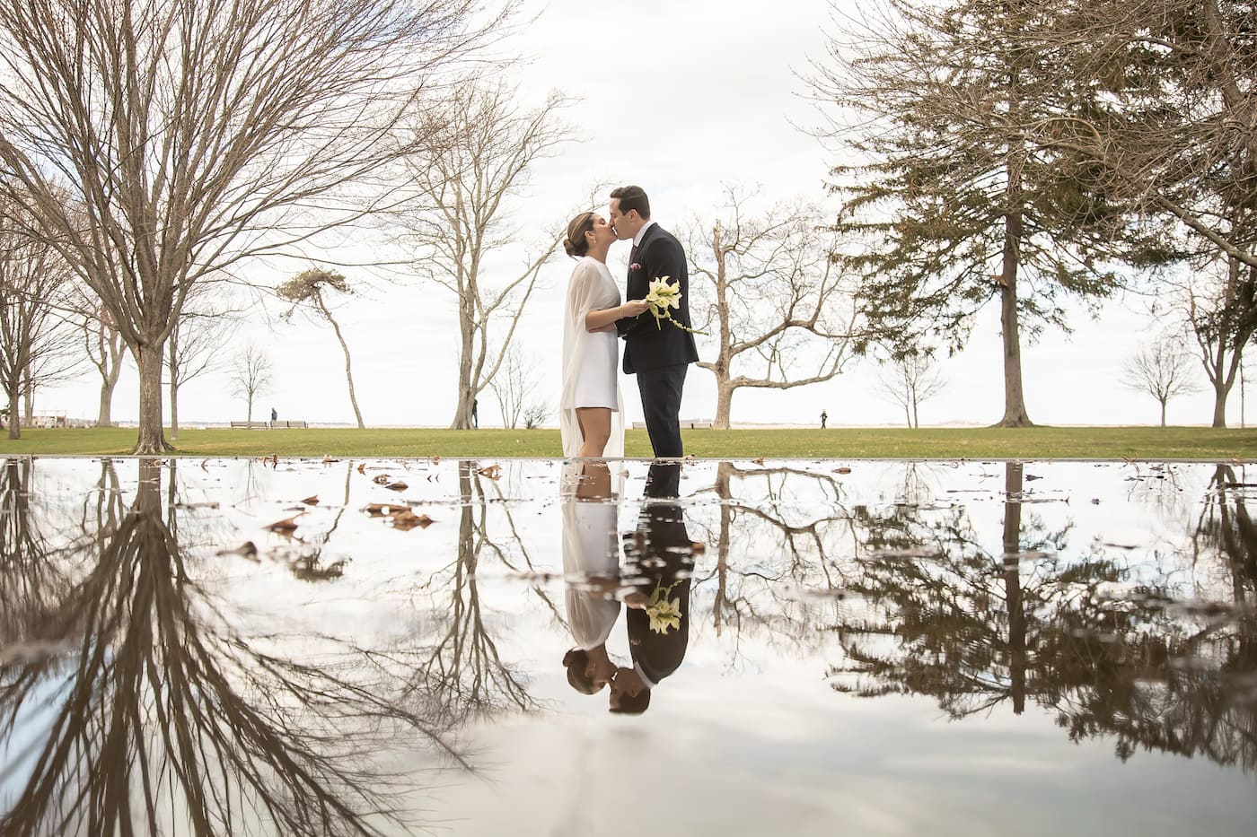 A creative wedding portrait of a bride and groom kissing with their reflection mirrored in a puddle before them, featured on Spagnolo Photography's Micro Wedding Packages page