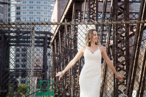 A bride stands in front of a chain-link fence in Boston's seaport, photographed by Spagnolo Photography as part of a micro-wedding package that included ceremony coverage on the Odyssey Cruise