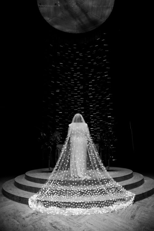 A bride on the stairs of the MIT Chapel altar, facing away from the camera, showing off the back of her dress and her long polka dot veil, photographed as part of her micro-wedding photography package by Spagnolo Photography.