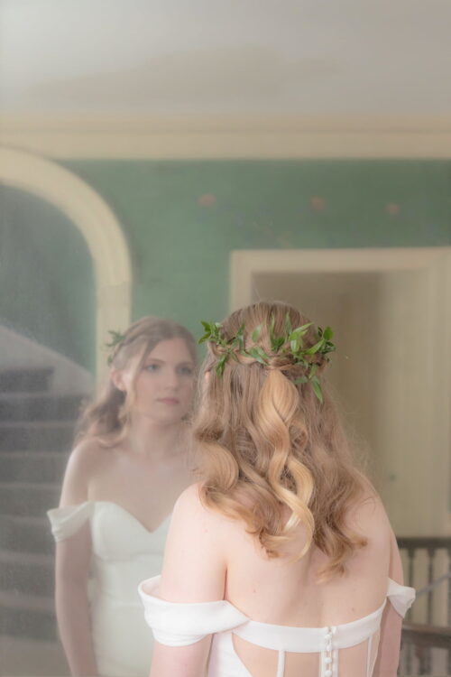 A dreamy and romantic photograph of a bride with a leaf crown staring at herself in a silvered mirror at the Long Hill Estate in Beverly, MA - photographed by creative wedding photographers Spagnolo Photography for her micro-wedding photography package.